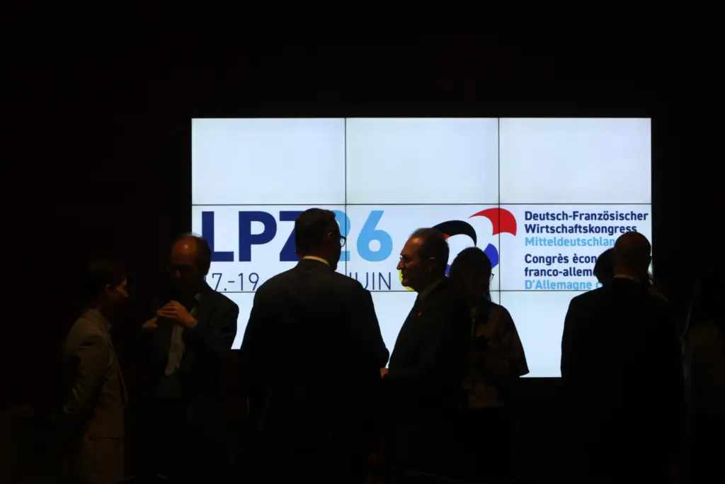 Im Gegenlicht aufgenommene Silhouetten von Kongressteilnehmern, die sich zum Ausklang des 3. Deutsch-Französischen Wirtschaftskongresses Mitteldeutschland (LPZ26) in Leipzig vor einer leuchtenden Medienwand unterhalten. Foto: Anja Jungnickel