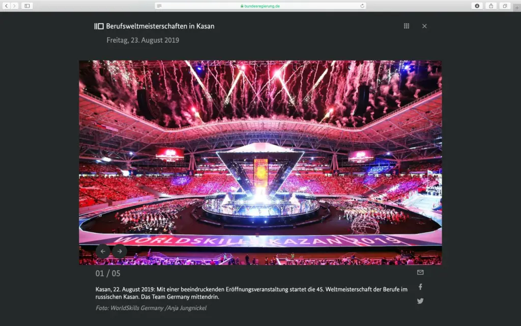 Screenshot der Webseite bundesregierung.de mit der Überschrift "Berufsweltmeisterschaften in Kasan" vom 23. August 2019. Im Zentrum steht ein großformatiges Foto von Anja Jungnickel, das die spektakuläre Eröffnungsveranstaltung der 45. Berufsweltmeisterschaft im russischen Kasan zeigt: Ein riesiges, voll besetztes Stadion mit rot beleuchteten Rängen, einer zentralen futuristischen Bühne und Feuerwerk am Himmel. Darunter steht der Bildtext zu Kasan vom 22. August 2019 und der offizielle Fotonachweis "Foto: WorldSkills Germany /Anja Jungnickel".