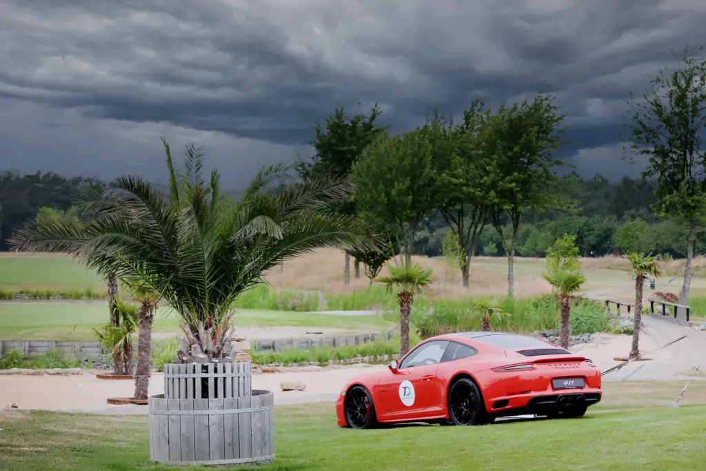 Professionelle Unternehmens- und Eventfotografie von Anja Jungnickel beim Porsche Golf Cup in Machern bei Leipzig: Ein roter Porsche 911 auf dem Golfplatz neben einer Palme vor dramatischem Wolkenhimmel[cite: 21].
