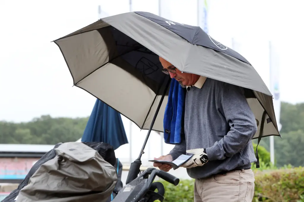 Professionelle Unternehmens- und Eventfotografie von Anja Jungnickel beim Porsche Golf Cup in Machern bei Leipzig: Ein Golfer prüft geschützt unter einem Regenschirm seine Scorecard[cite: 20].