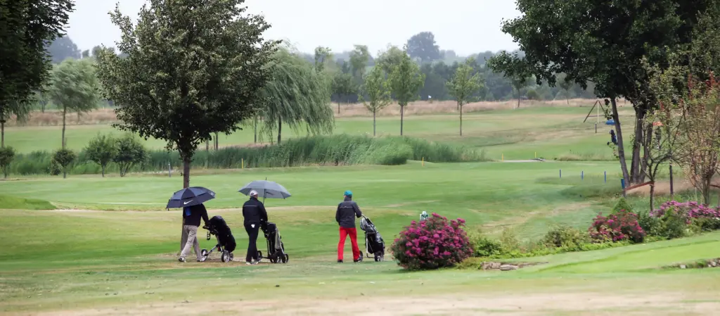 Professionelle Unternehmens- und Eventfotografie von Anja Jungnickel beim Porsche Golf Cup in Machern bei Leipzig: Golfer mit Regenschirmen und Trolleys gehen über den weitläufigen Golfplatz.