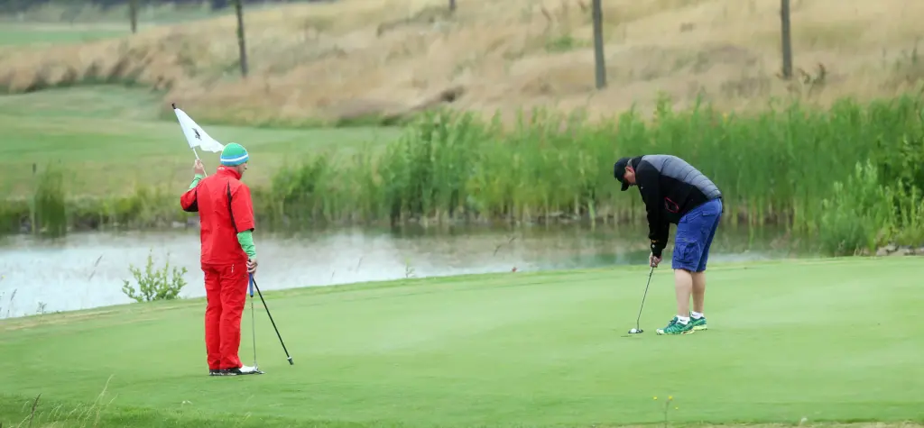 Professionelle Unternehmens- und Eventfotografie von Anja Jungnickel beim Porsche Golf Cup in Machern bei Leipzig: Ein Golfer puttet auf dem Grün nahe einem Gewässer, während ein Teilnehmer die Fahne hält[cite: 17].