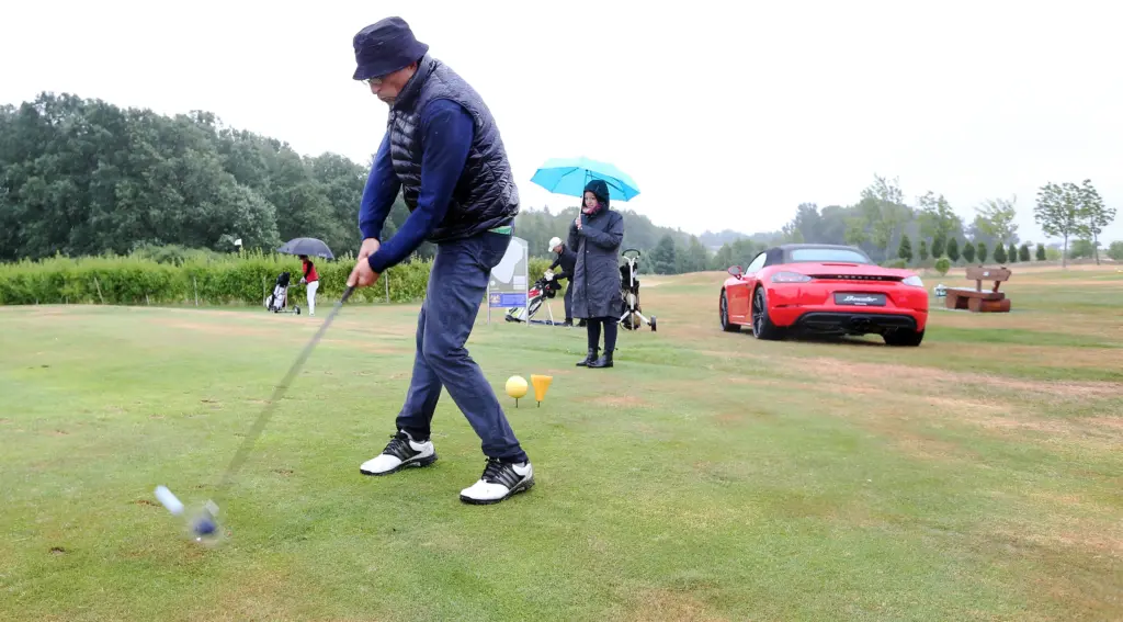 Professionelle Unternehmens- und Eventfotografie von Anja Jungnickel beim Porsche Golf Cup in Machern bei Leipzig: Ein Golfer schlägt ab, während im Hintergrund ein roter Porsche Sportwagen als Sponsorenfahrzeug steht[cite: 24].