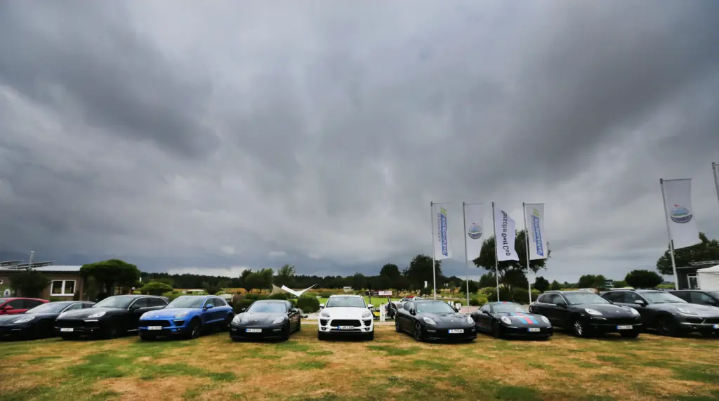 Professionelle Unternehmens- und Eventfotografie von Anja Jungnickel beim Porsche Golf Cup in Machern bei Leipzig: Eine Reihe geparkter Porsche-Fahrzeuge auf einer Rasenfläche unter dramatischem Wolkenhimmel.