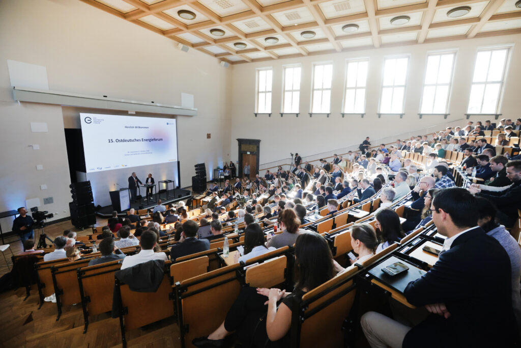 Hochwertige Business- und Eventfotografie vom 15. Ostdeutschen Energieforum in Leipzig, festgehalten von Anja Jungnickel. Das Bild zeigt Dietrich Enk (Präsident des Unternehmerverbandes Sachsen) mit Mikrofon gestikulierend auf der Bühne, während Moderatorin Andrea Thilo ihm am Stehtisch aufmerksam und lächelnd zuhört. Perfekt als Referenz für hochkarätige Konferenzfotografie, Wirtschaftsgipfel und professionelle Unternehmensfotografie.